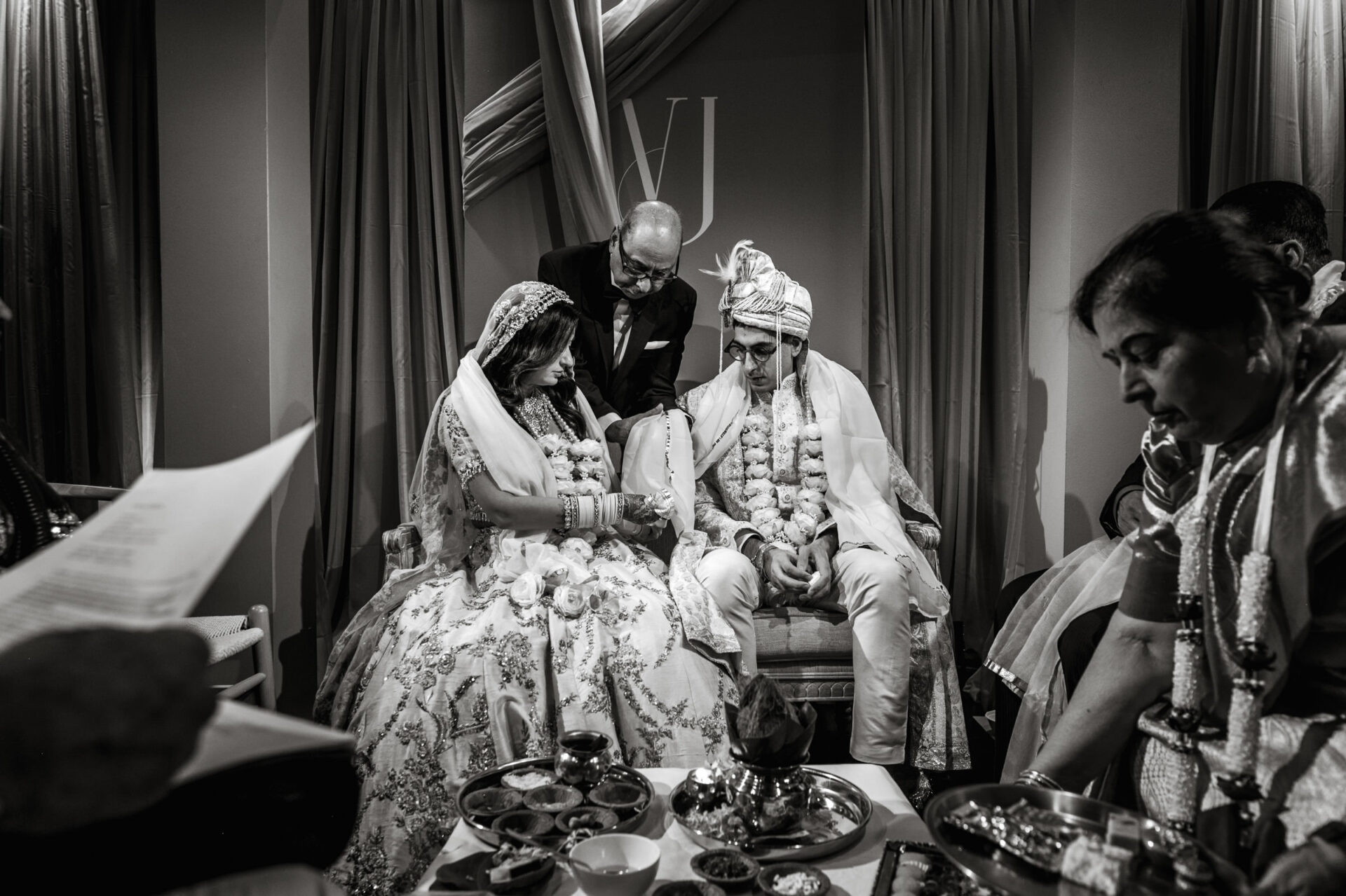 A couple in traditional attire at an indoor Sikh wedding with guests.