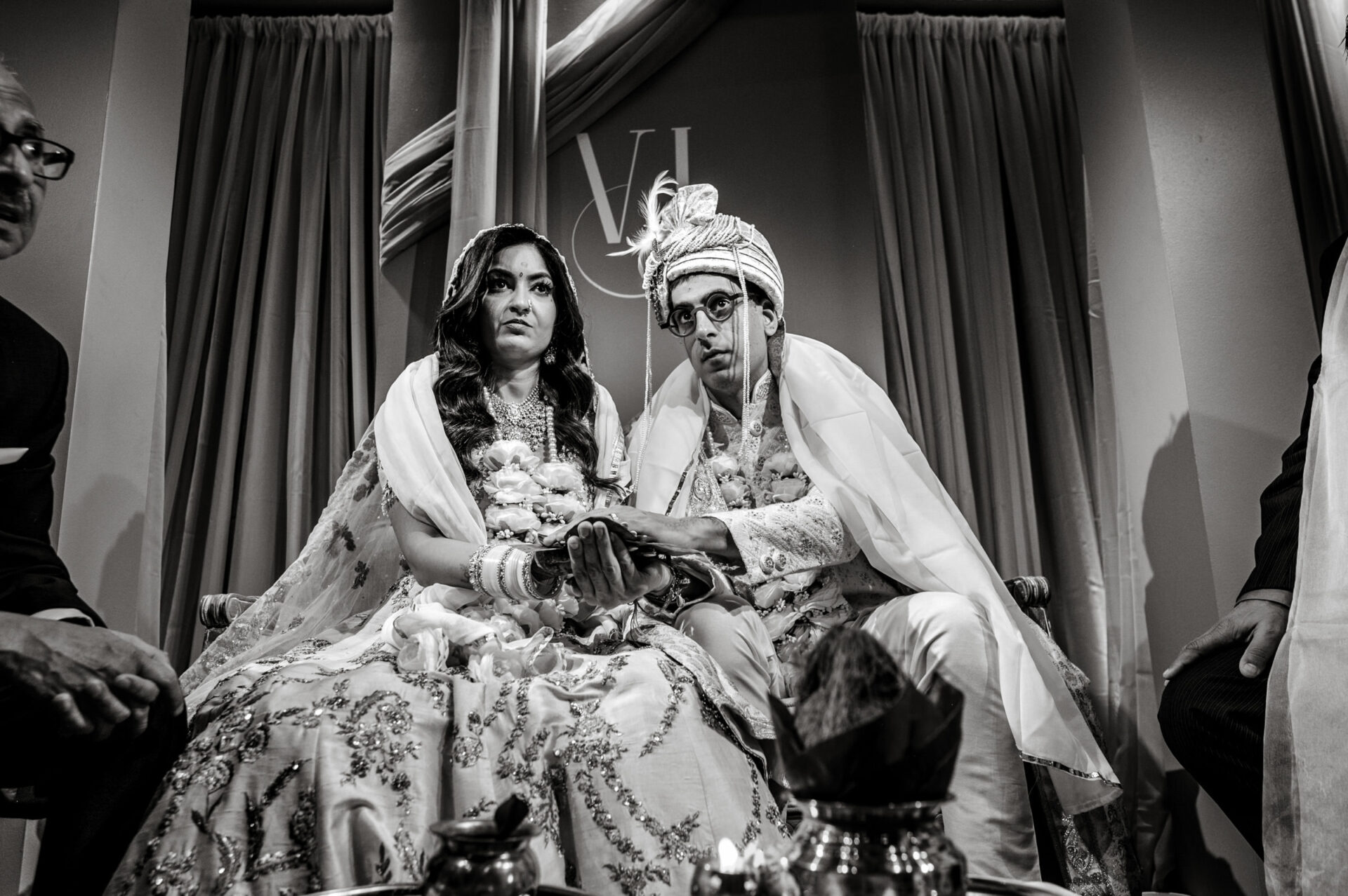 Bride and groom in traditional Sikh attire during a wedding, holding hands solemnly.