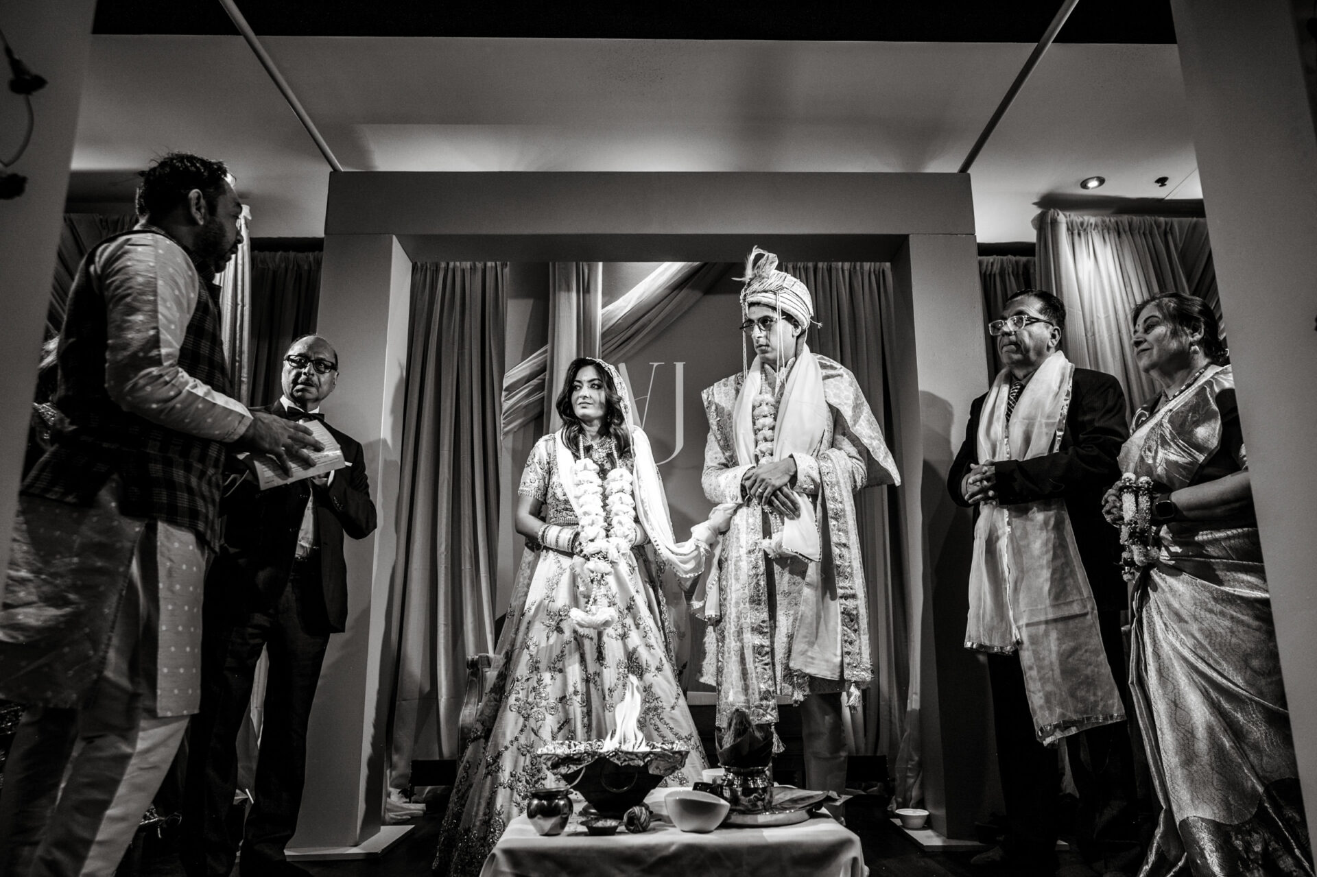 A couple in traditional attire at a Sikh wedding ceremony with four others present.