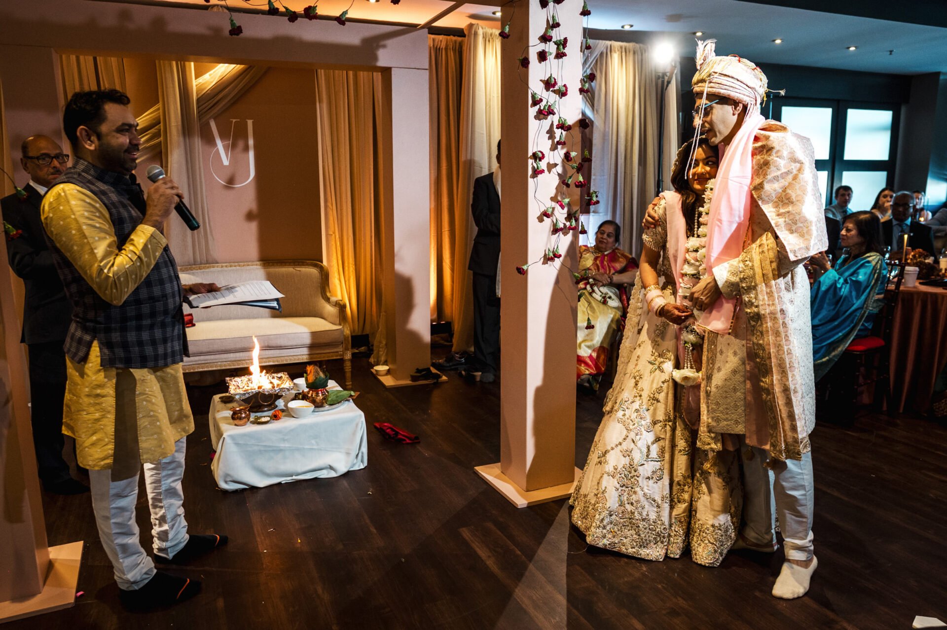 A couple in Sikh attire at a wedding ceremony with guests watching.