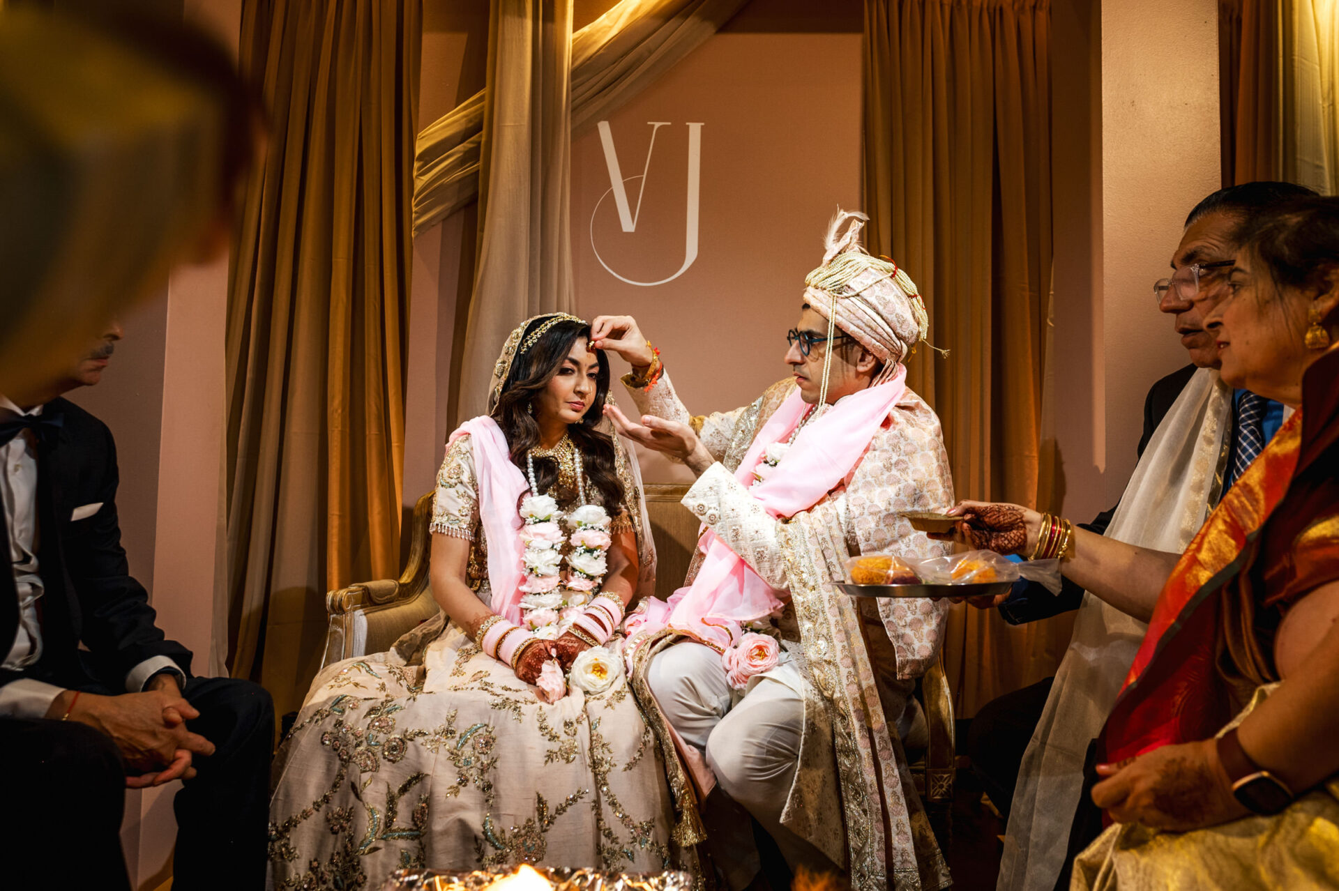 A Sikh couple in traditional attire during a wedding, surrounded by family members.