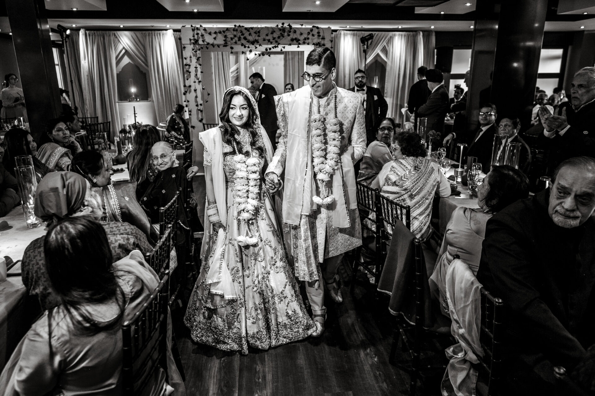 A couple in traditional attire walks hand in hand at their Sikh wedding reception.