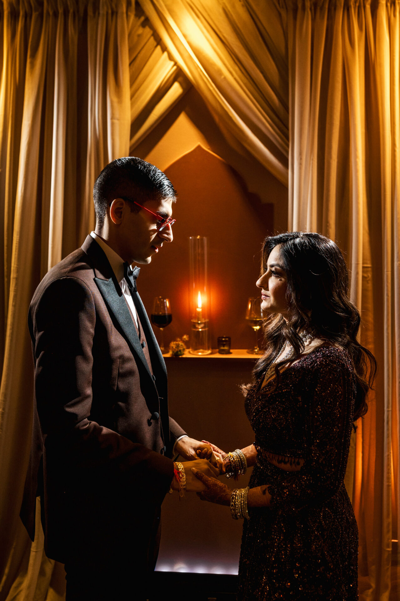 A couple in elegant attire holds hands under warm lights, embracing their Sikh wedding.