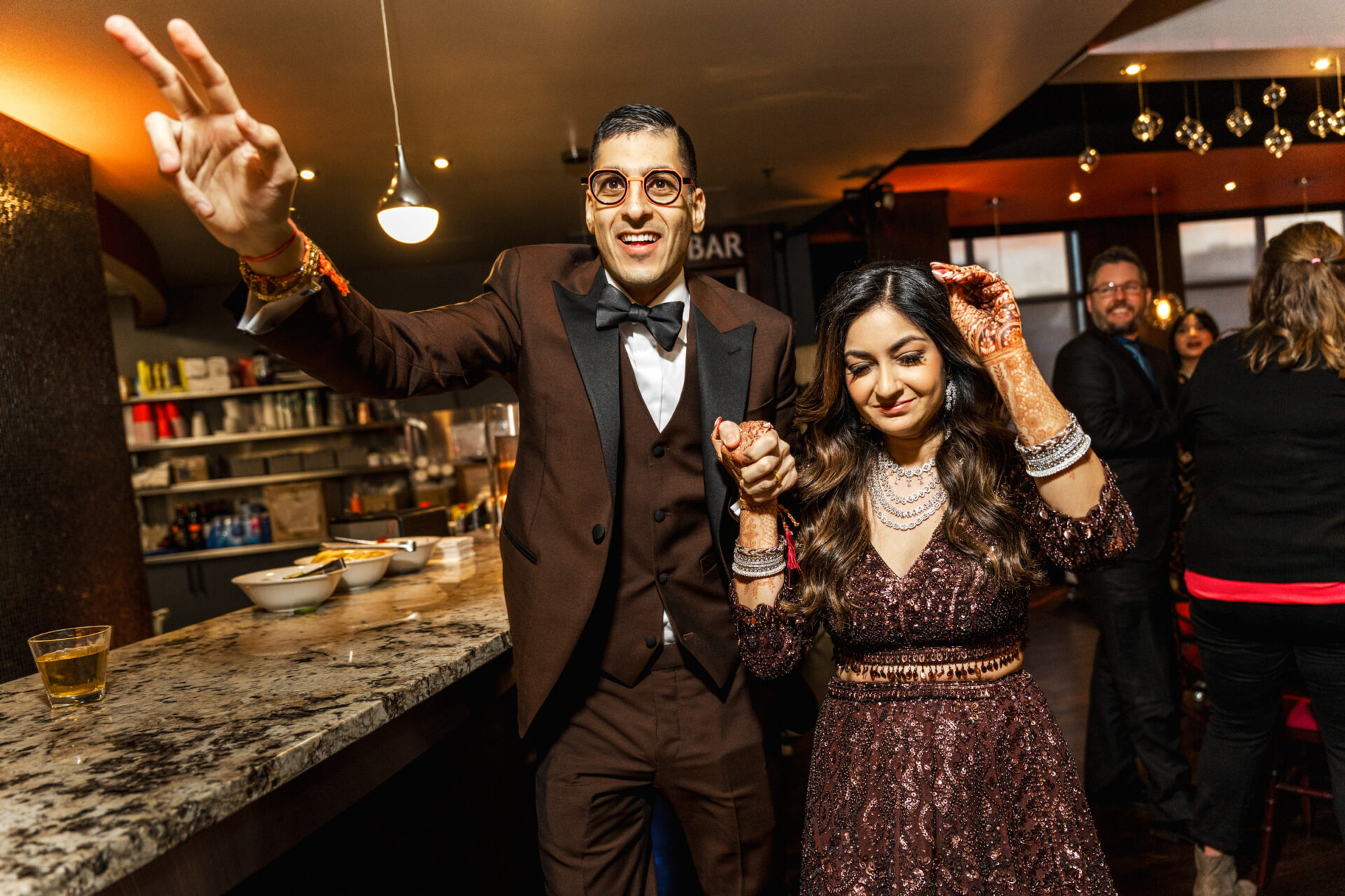 A smiling couple in formal attire celebrating at a lively Sikh wedding.