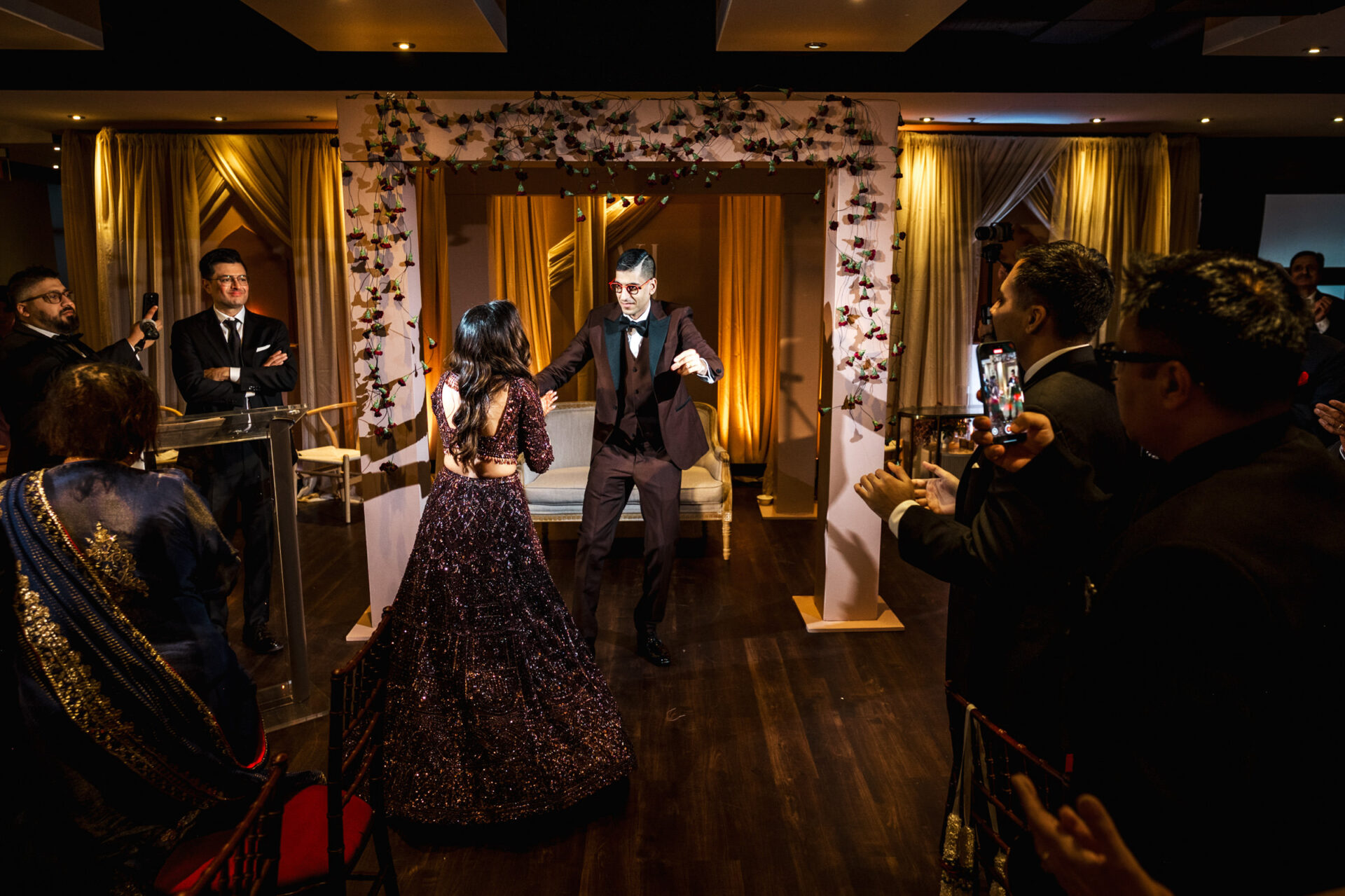 A couple dancing at a Sikh wedding celebration with guests applauding.
