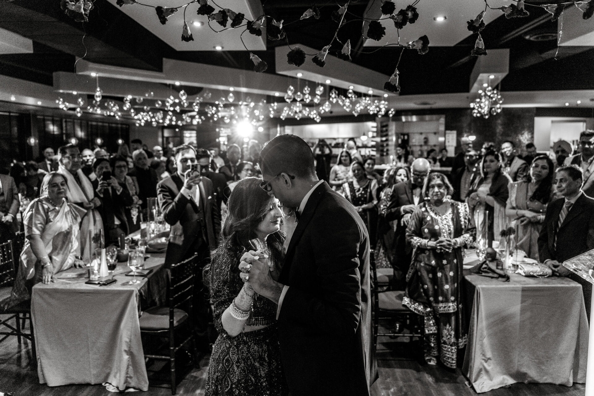 Couple dancing at their Sikh wedding, surrounded by guests in an elegantly lit venue.