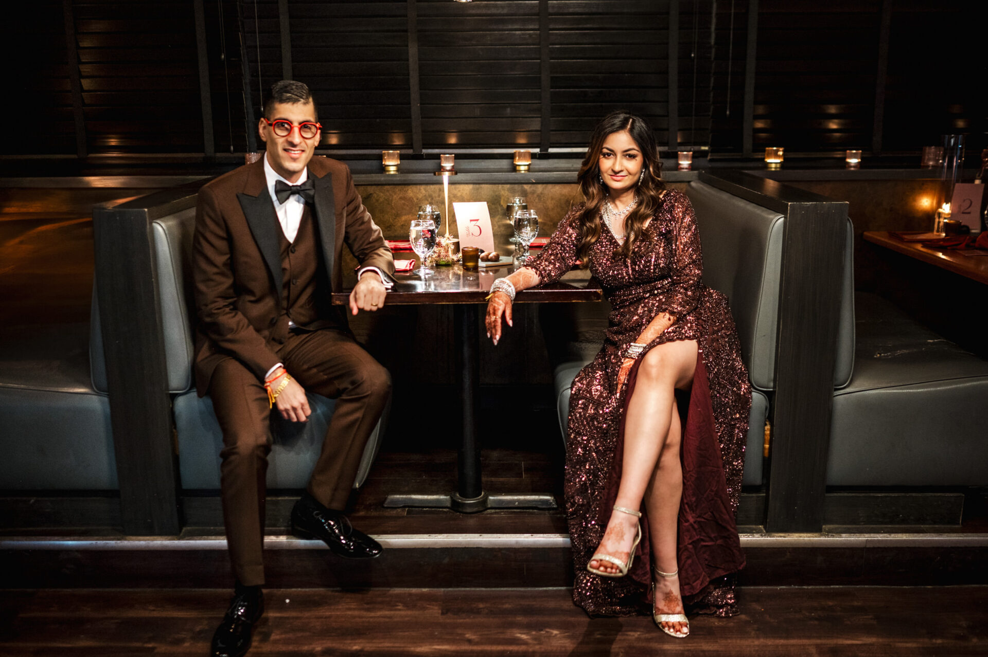 Couple in formal attire at a restaurant booth, celebrating a Sikh wedding under dim lighting.
