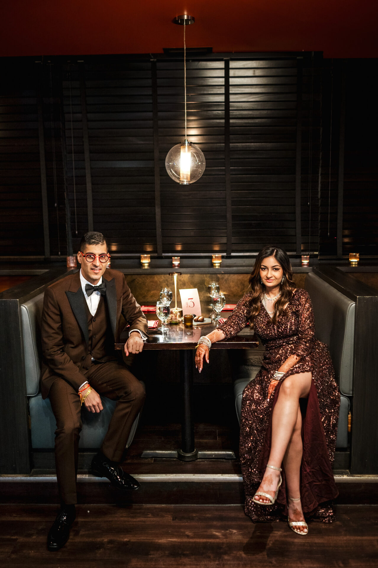 Couple in formal attire seated in a dimly lit booth at a Sikh wedding with table number 3.