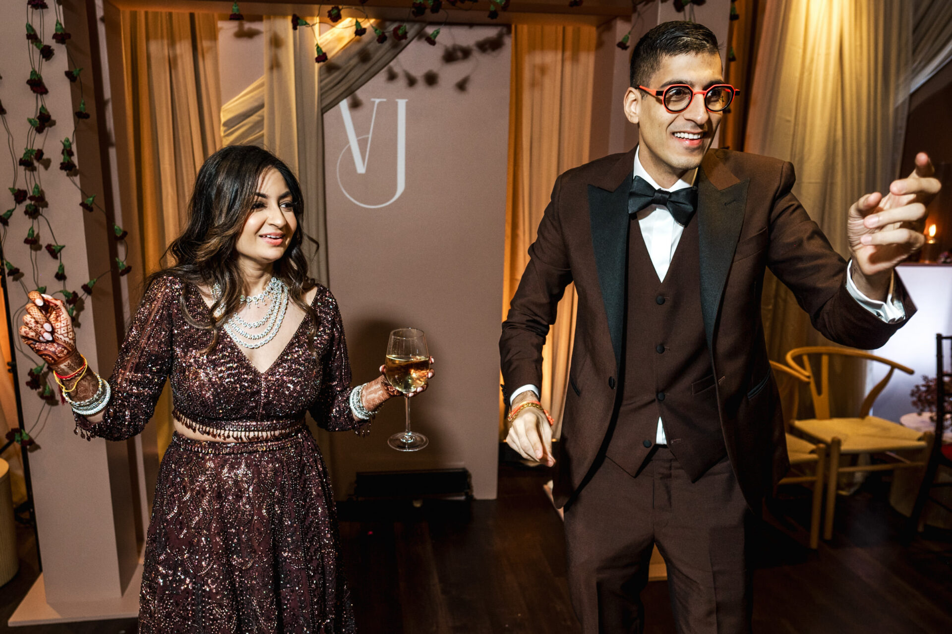 A couple in formal wear joyfully dances at a vibrant Sikh wedding celebration.
