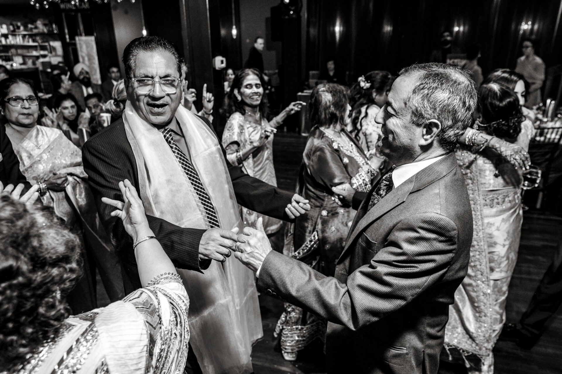 People in formal attire joyfully dancing at a lively Sikh wedding event.