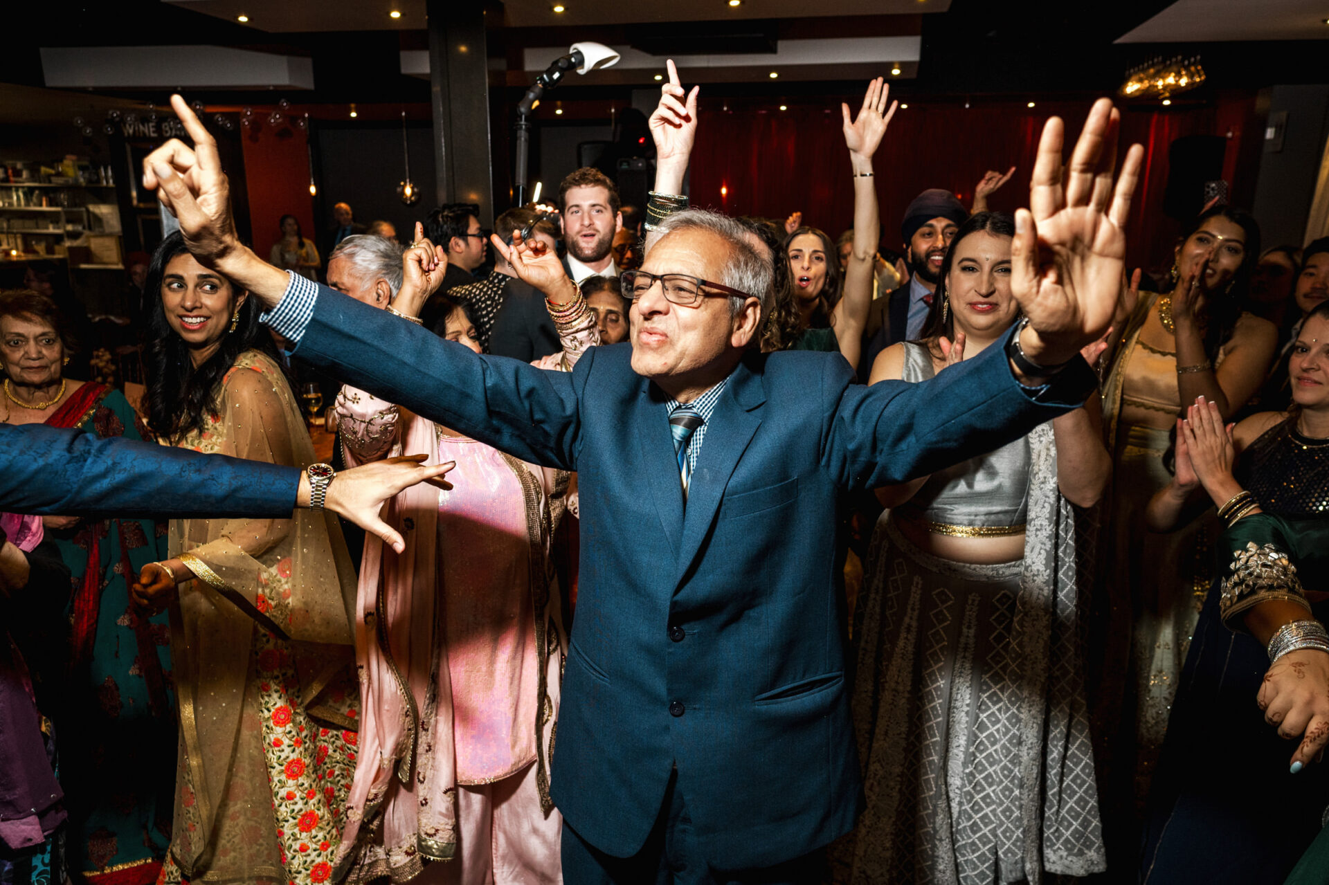 A man in a suit joyfully dances at a lively Sikh wedding party.