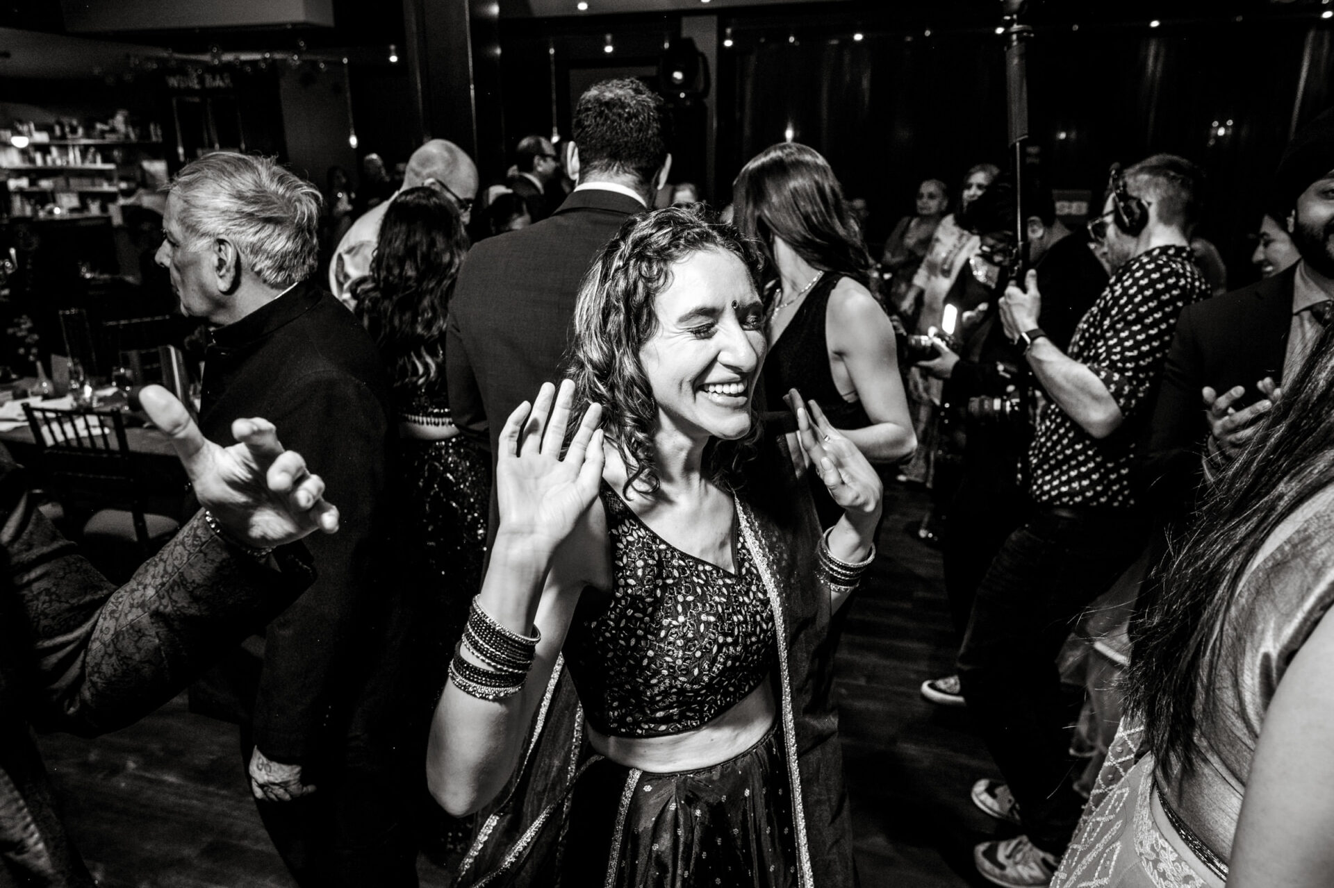 Woman joyfully dancing with raised hands at a lively Sikh wedding party.