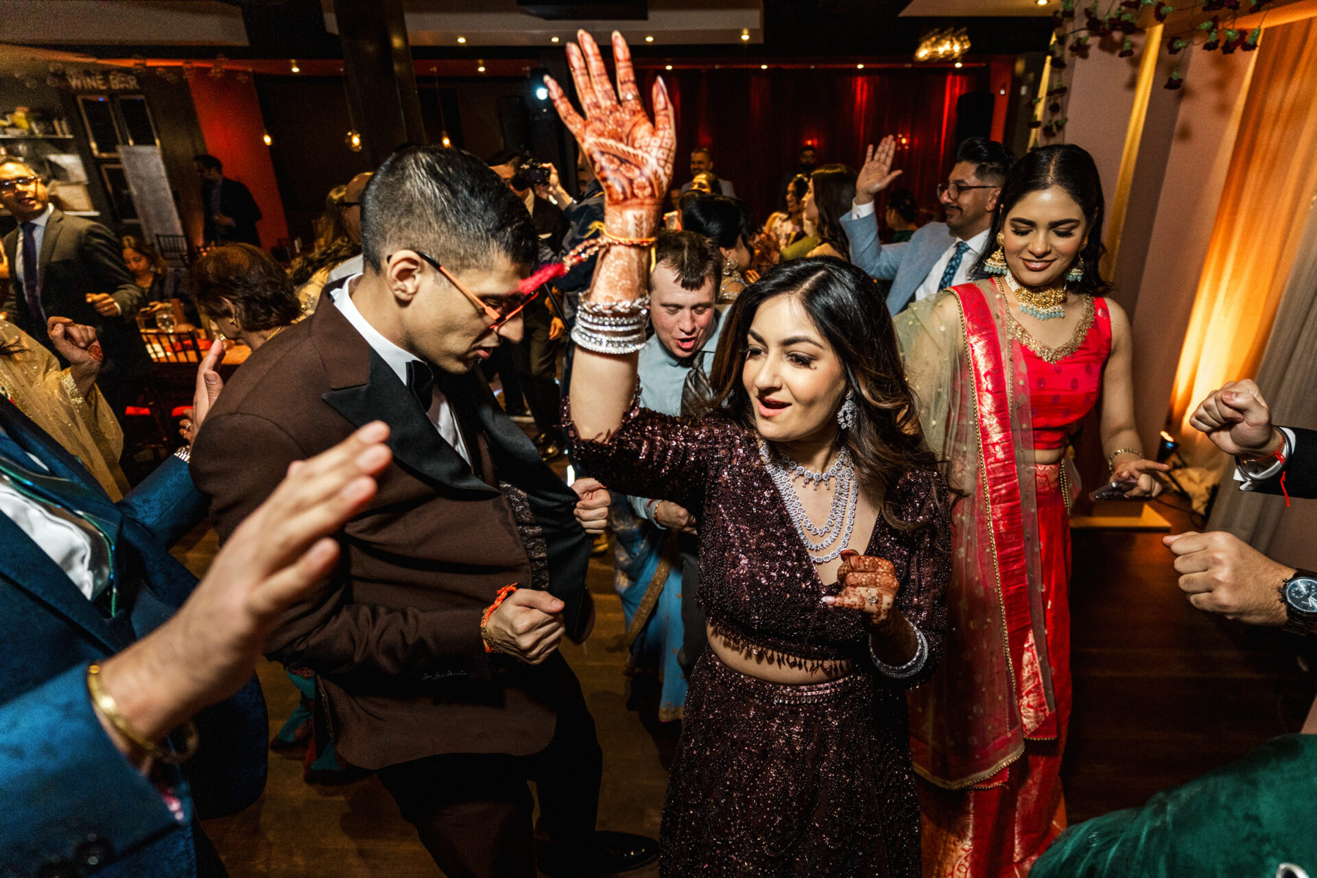 Guests dance energetically at a festive Sikh wedding, dressed in colorful attire.