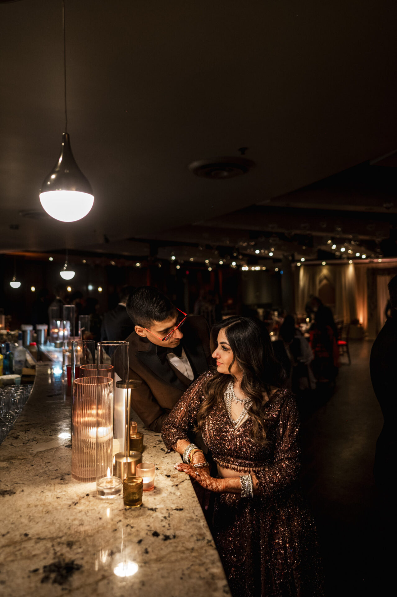 Couple at a bar with soft lighting, in formal attire, echoes of Sikh & Hindu wedding vibes.
