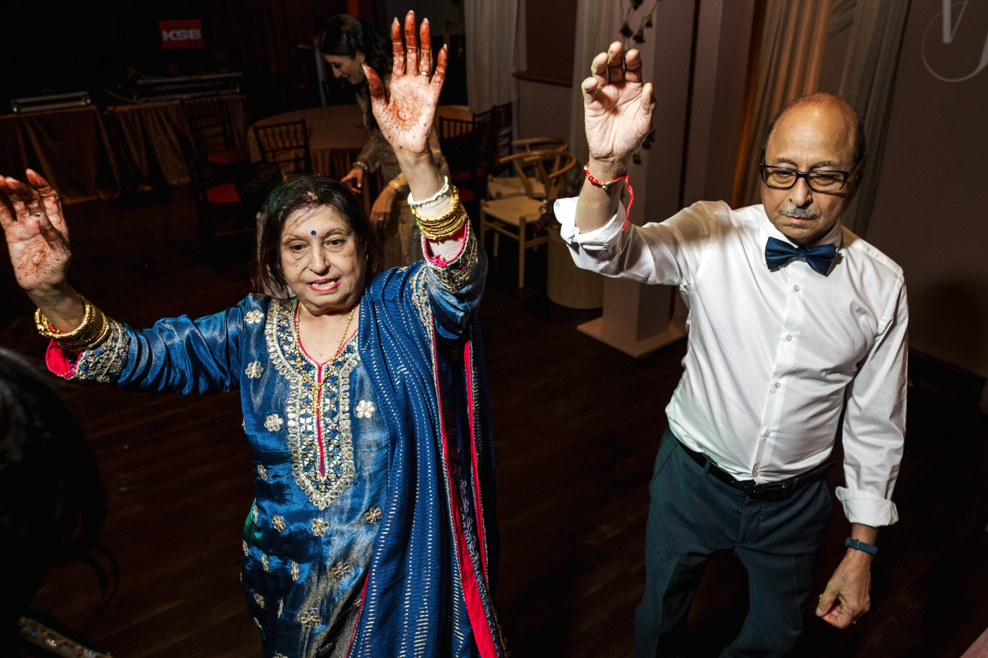 A Sikh wedding scene: two people dancing, in festive attire, celebrating with raised hands.