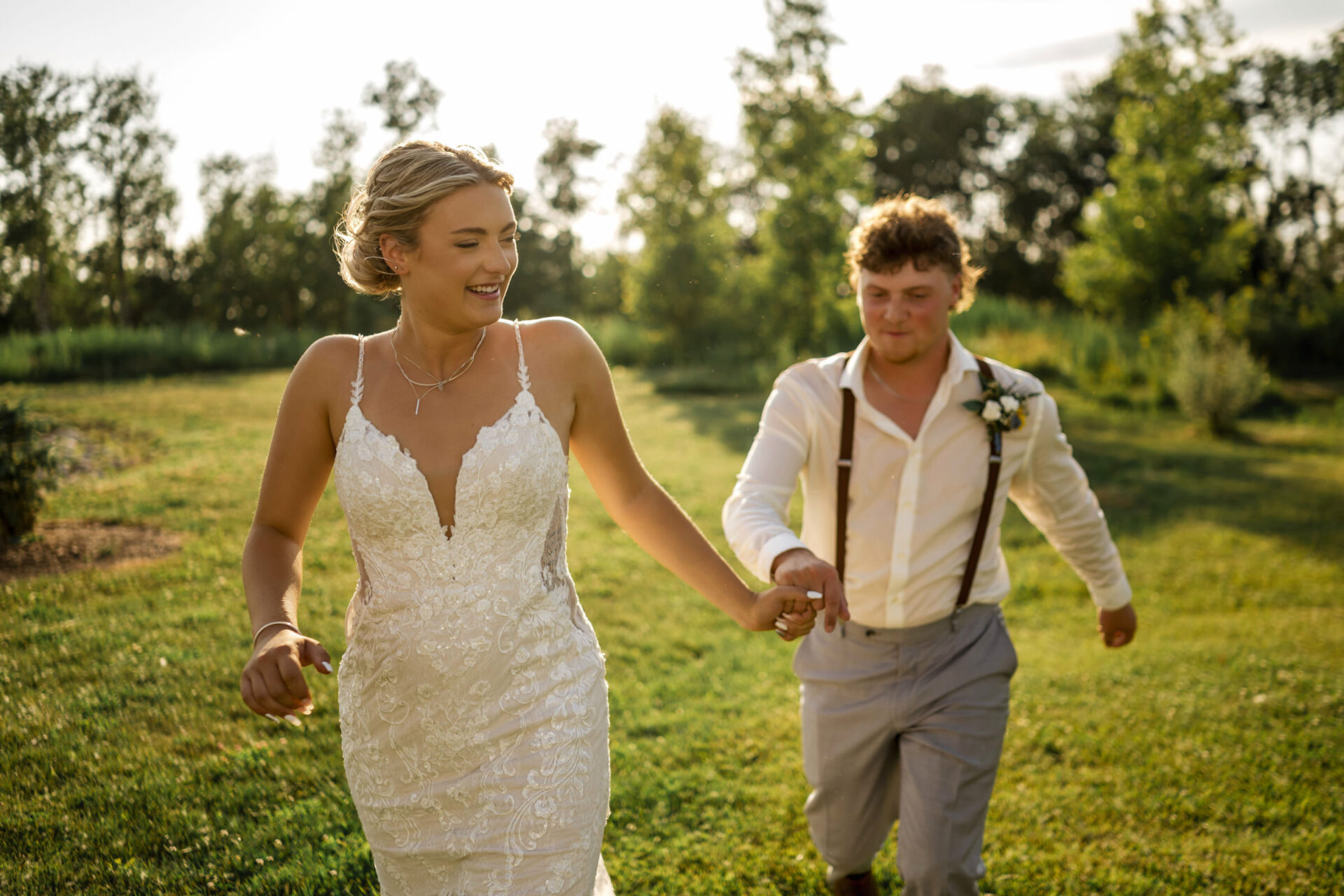 Bride and groom holding hands and running joyfully outside on a sunny day.
